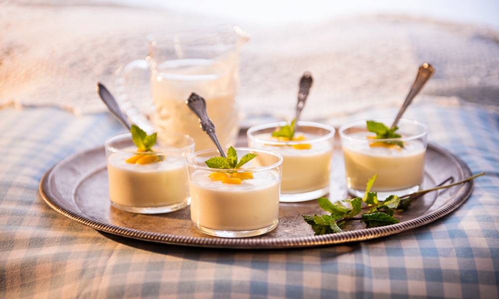 Fyra glas med pannacotta toppade med frukt och mynta på en metallbricka