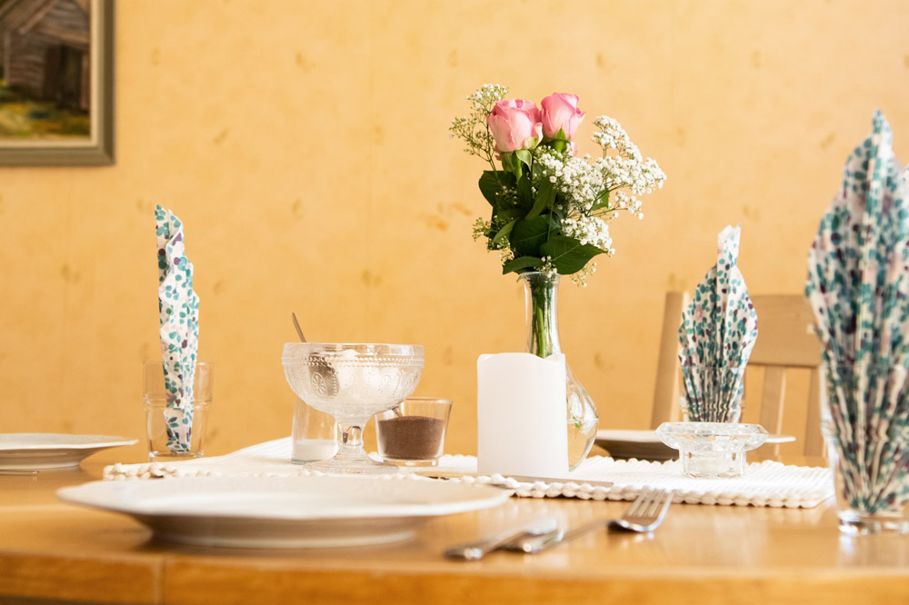 Dukat bord med rosor i vas och hopvikta servetter i mönstrade glas, ljus stämning