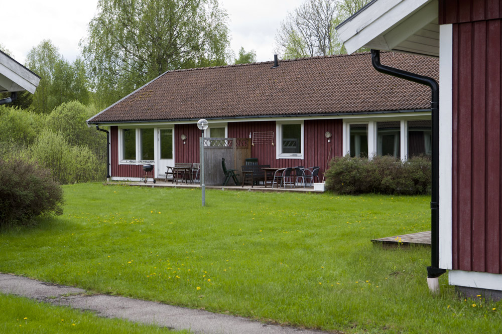 Röd trästuga i lantlig miljö med grönt gräs och omgivande skog