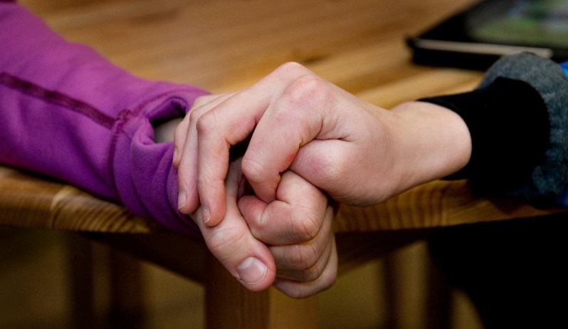 Två personer håller varandra i handen vid ett bord, symboliserar stöd och gemenskap