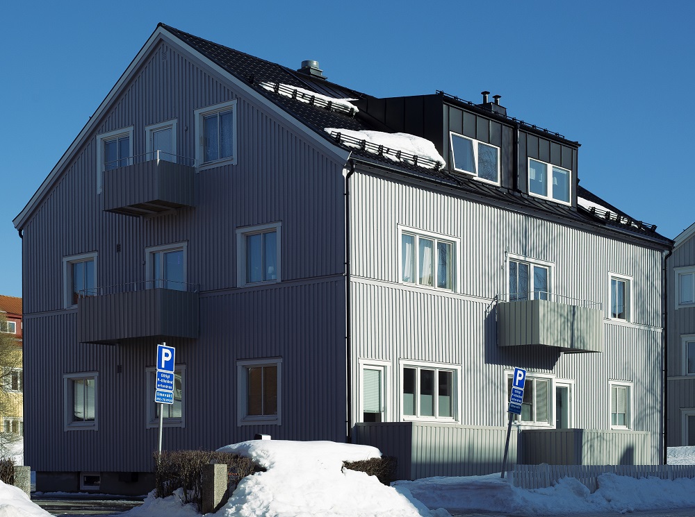 Grått flerfamiljshus i modern skandinavisk stil med balkonger och snötäckt tak, beläget i ett bostadsområde med snö på marken