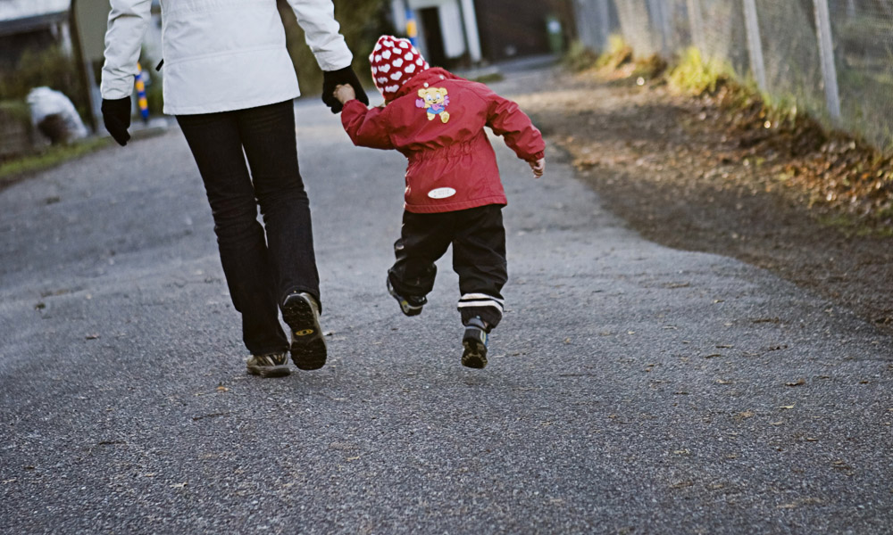 Ett skuttande barn håller en vuxen i handen när de promenerar på en gångväg, båda iförda vinterkläder 