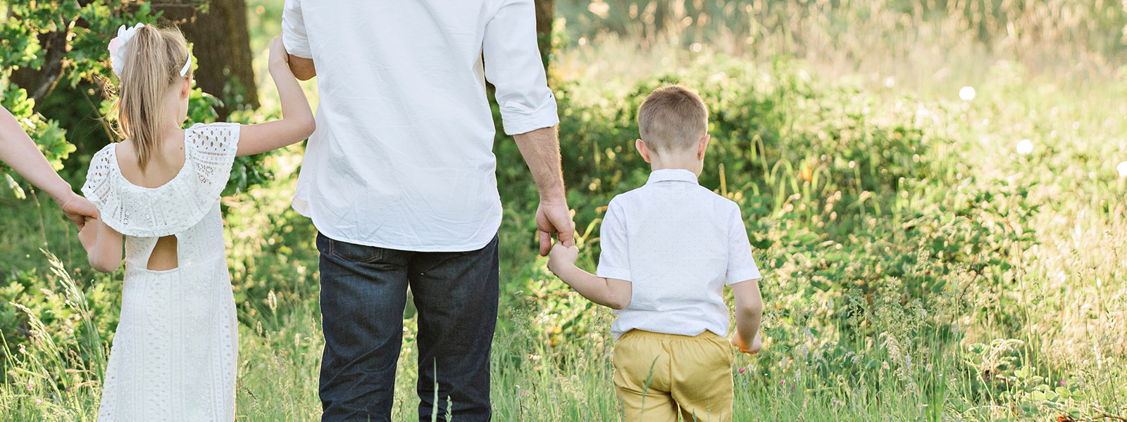 En vuxen och ett barn går hand i hand i en höstig park, omgivna av gyllene löv och soliga träd