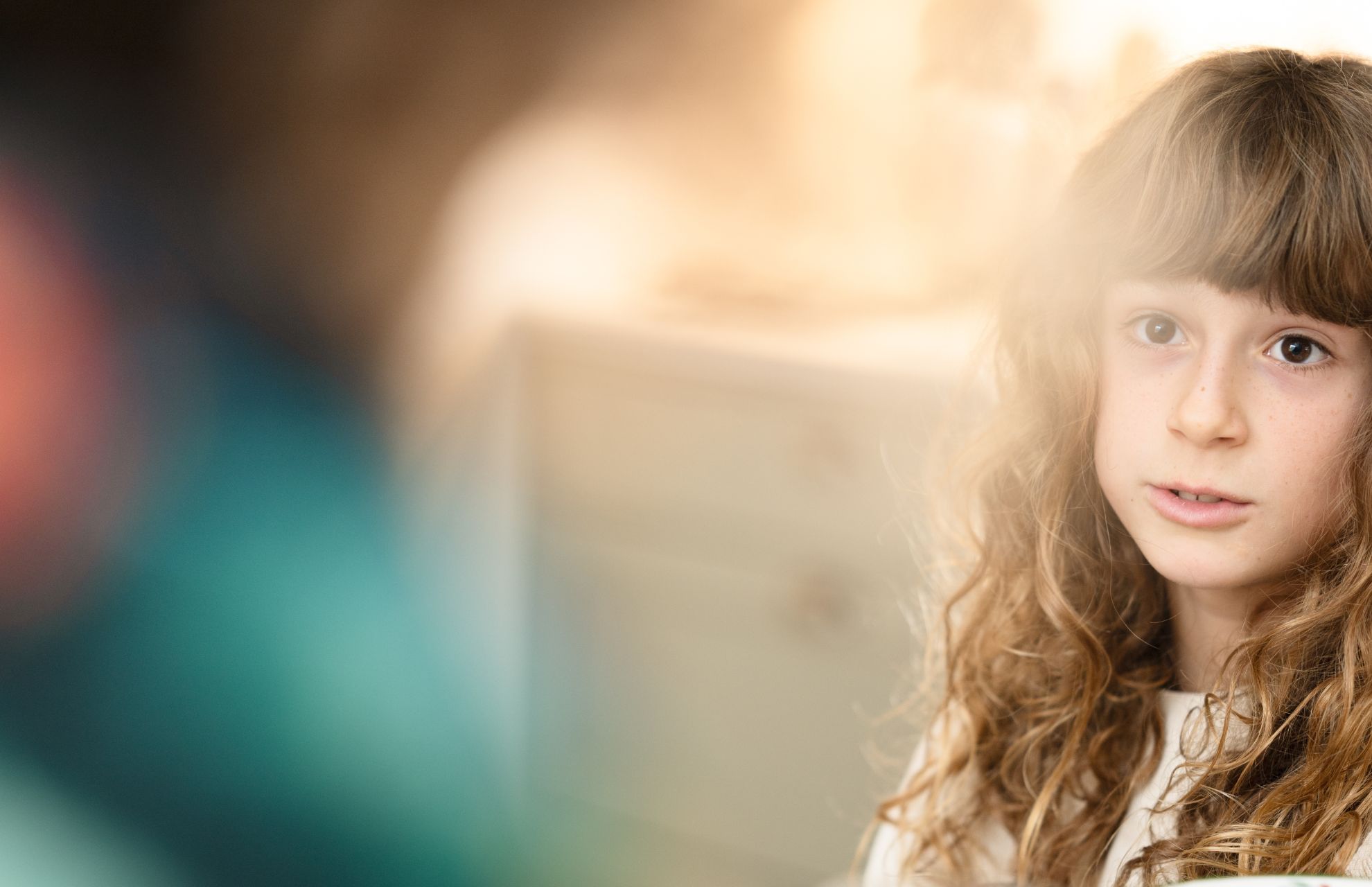 Ung flicka med långt lockigt hår i mjuk fokus, sittande i ett ljust rum