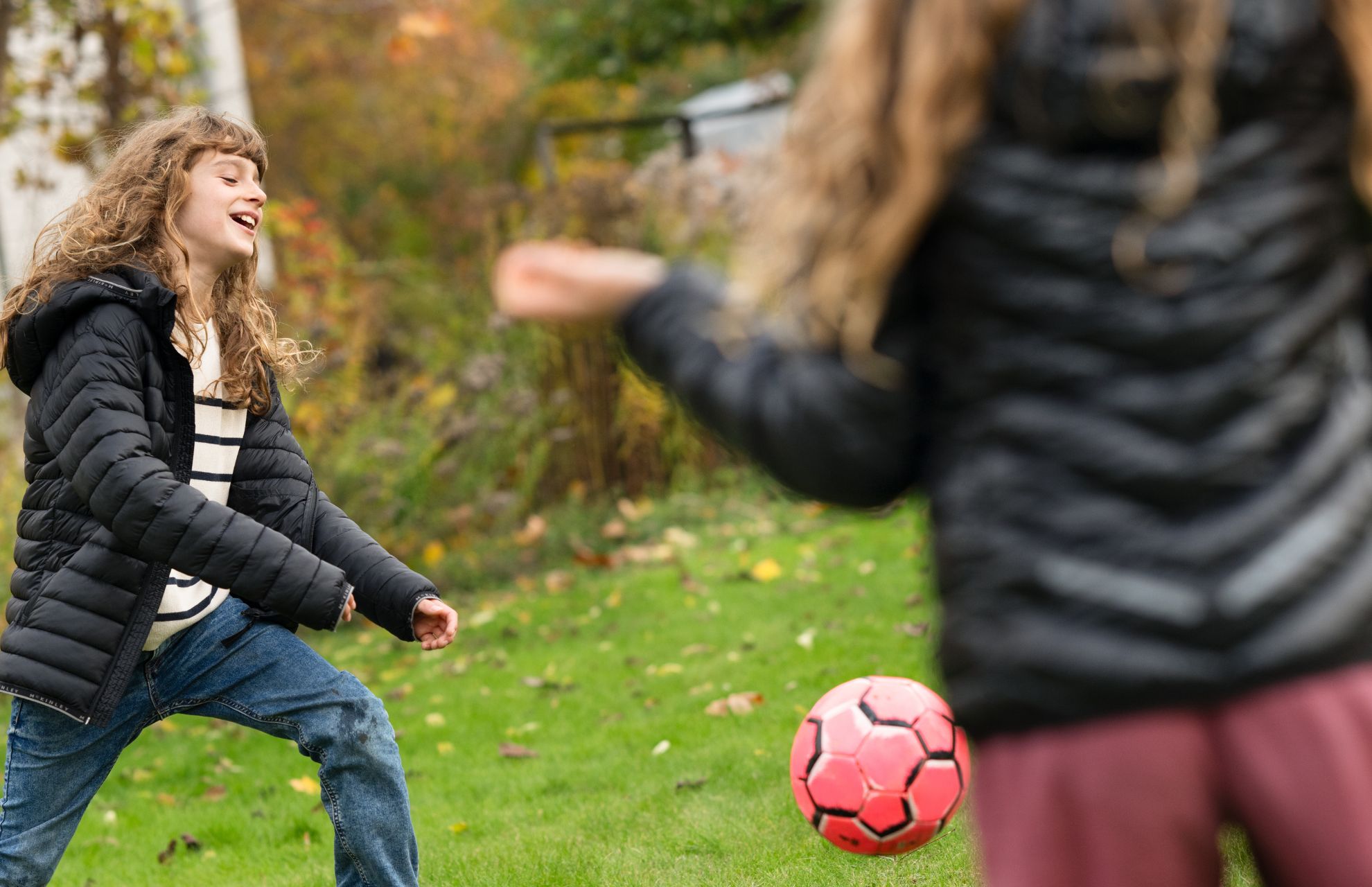 Man kastar en fotboll till ett barn i en trädgård, inramad av häckar och en lantlig bakgrund