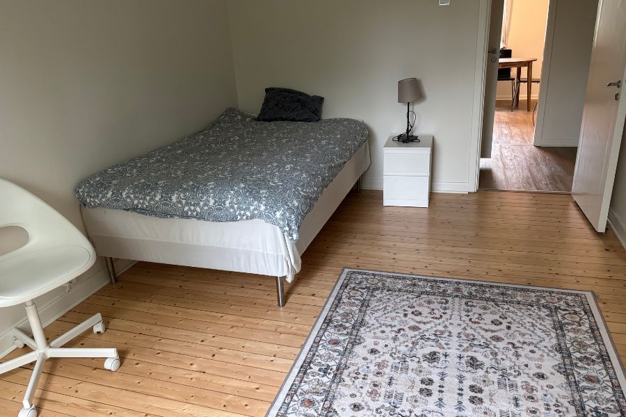 Säng med sängbord, stol och matta i sovrumsdel