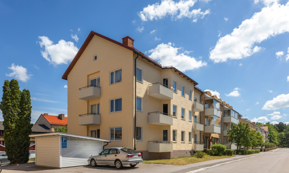 Flerfamiljshus i Sverige med gul fasad och balkonger, solig dag med blå himmel och vita moln