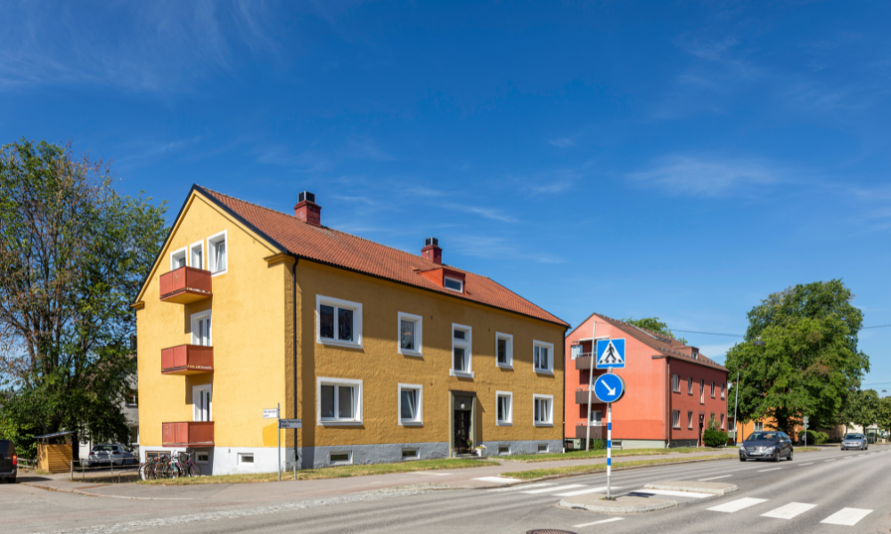 Gula och röda flerbostadshus vid en gata med övergångsställe och bilar under en klarblå himmel