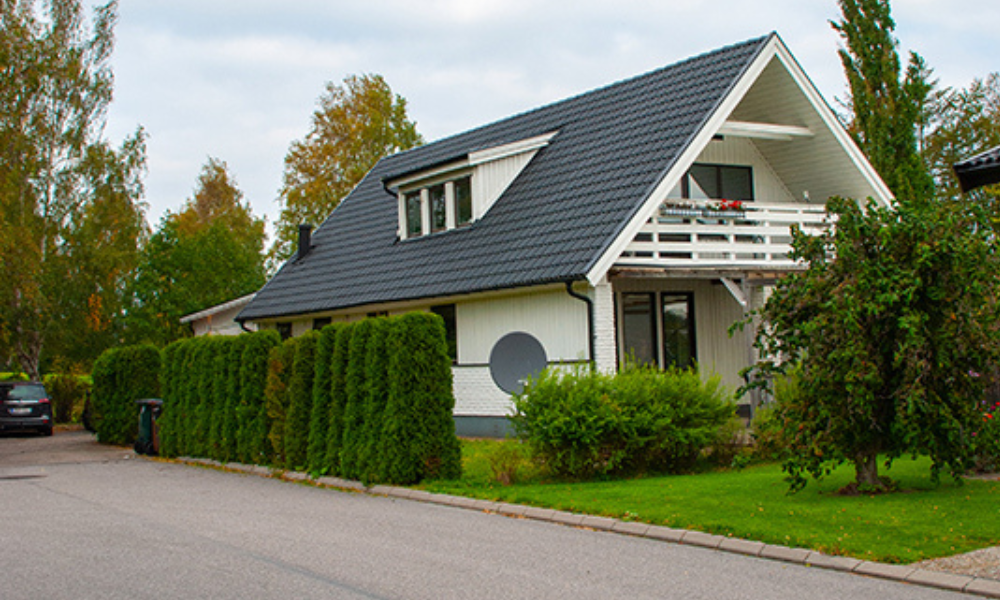 Vit modern villa med grått snedtak i ett lugnt svenskt bostadsområde, omgiven av träd och en välskött gräsmatta